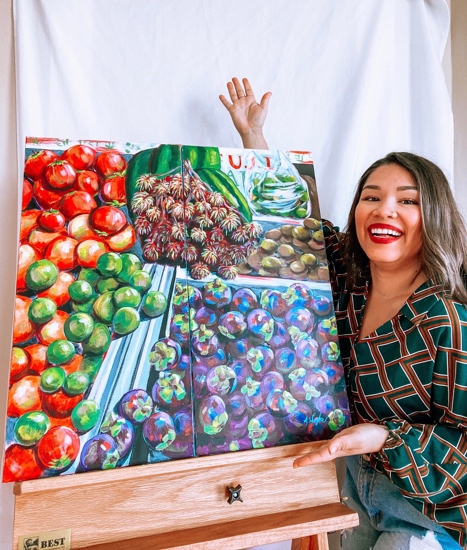 Alexandra Wuyke, St. Pete Acrylic Artist stands next to an original painting of a fruit stand in bold vibrant colors. 