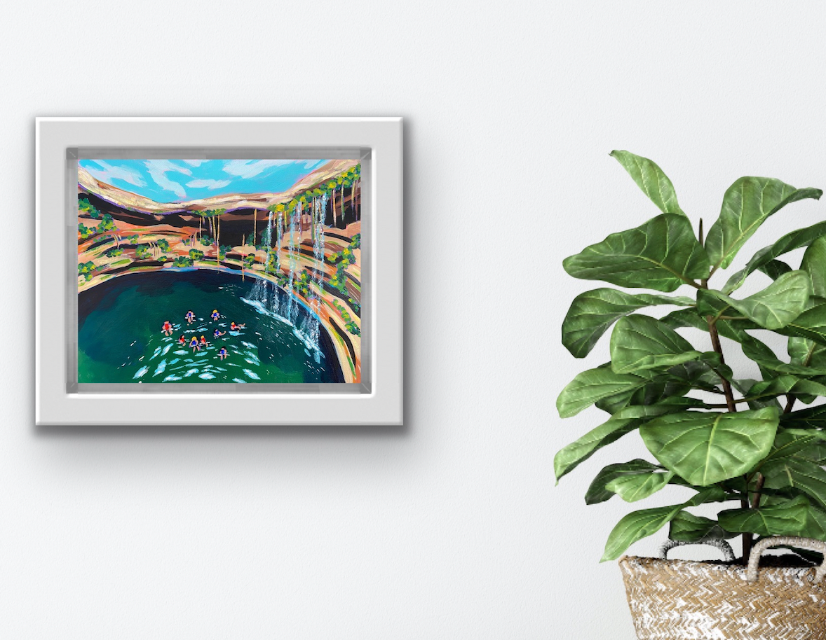 Travel Art "Cenotes" By Boston Artist Alexandra Wuyke hangs on a wall next to a plant. 